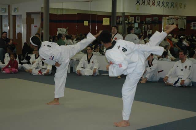 two taekwondo students in white gi high kicking on the mat